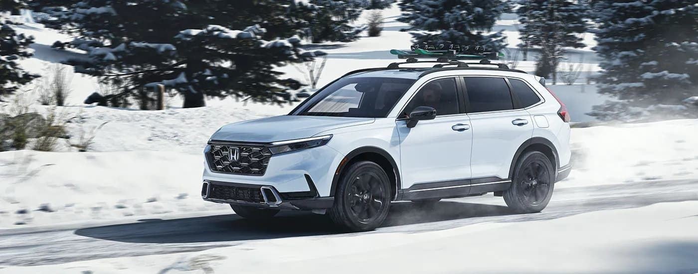 A white 2023 Honda CR-V Sport Touring Hybrid driving over a snowy road from a SUV dealership near Atlanta.