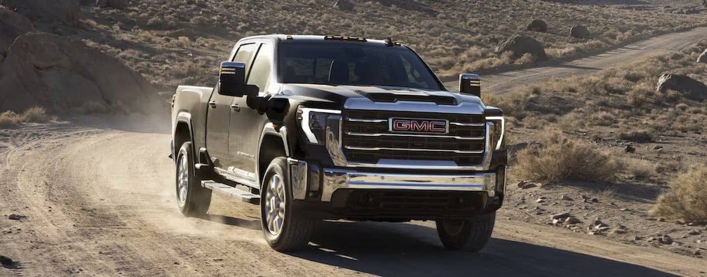 A black 2024 GMC Sierra 2500 HD is shown driving off-road after viewing work trucks for sale in Atlanta.
