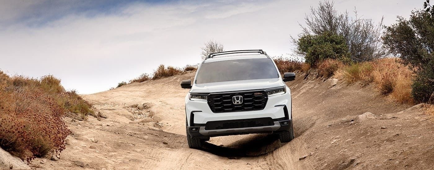 A front angle view of a white 2023 Honda Pilot TrailSport driving down a sandy hill.