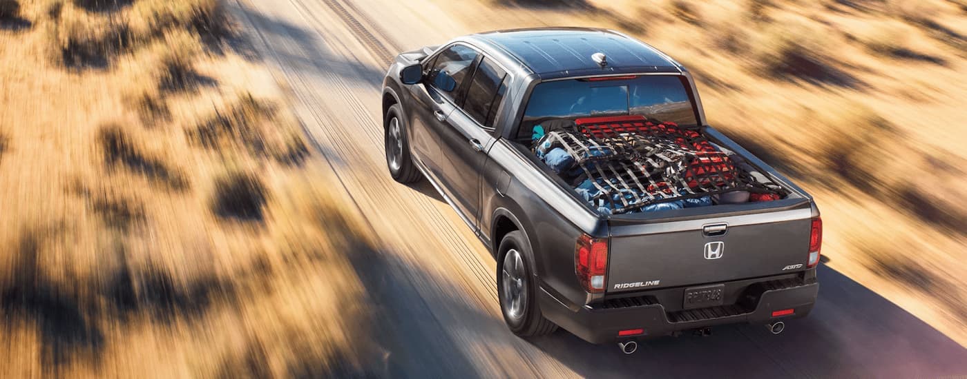A grey 2022 Honda Ridgeline is driving on a dusty dirt road with cargo in the bed.