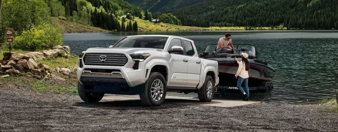 Left angled shot of a white 2024 Toyota Tacoma Limited towing a boat by a lake.