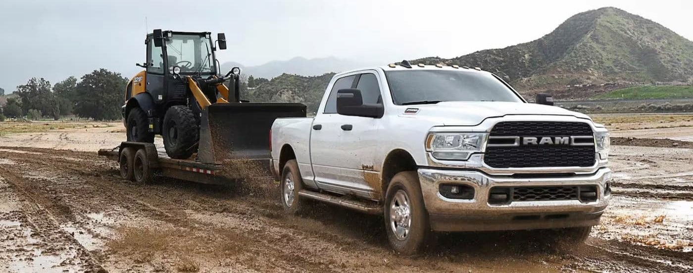 A white 2023 Ram 2500 Laramie is shown towing a trailer on mud.