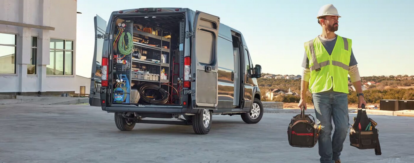 A utility worker walking away from a grey 2024 Ram ProMaster Cargo Van full of equipment.