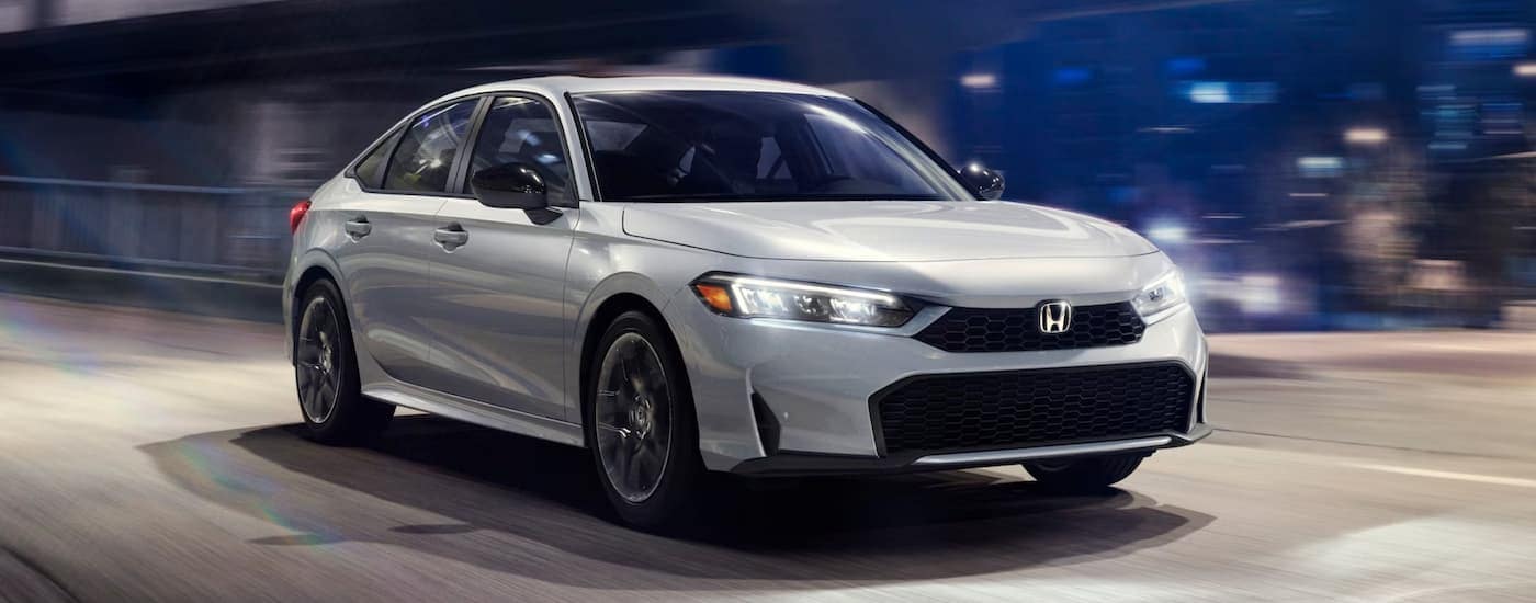 A white 2025 Honda Civic Sport Hybrid is leaving a car dealer near Suwanee.
