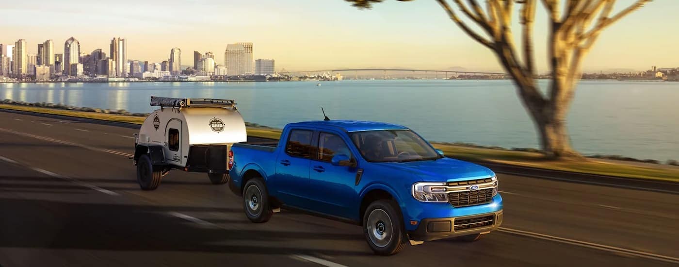 A blue 2023 Ford Maverick is towing a small camper trailer after leaving a truck dealership near Raleigh.