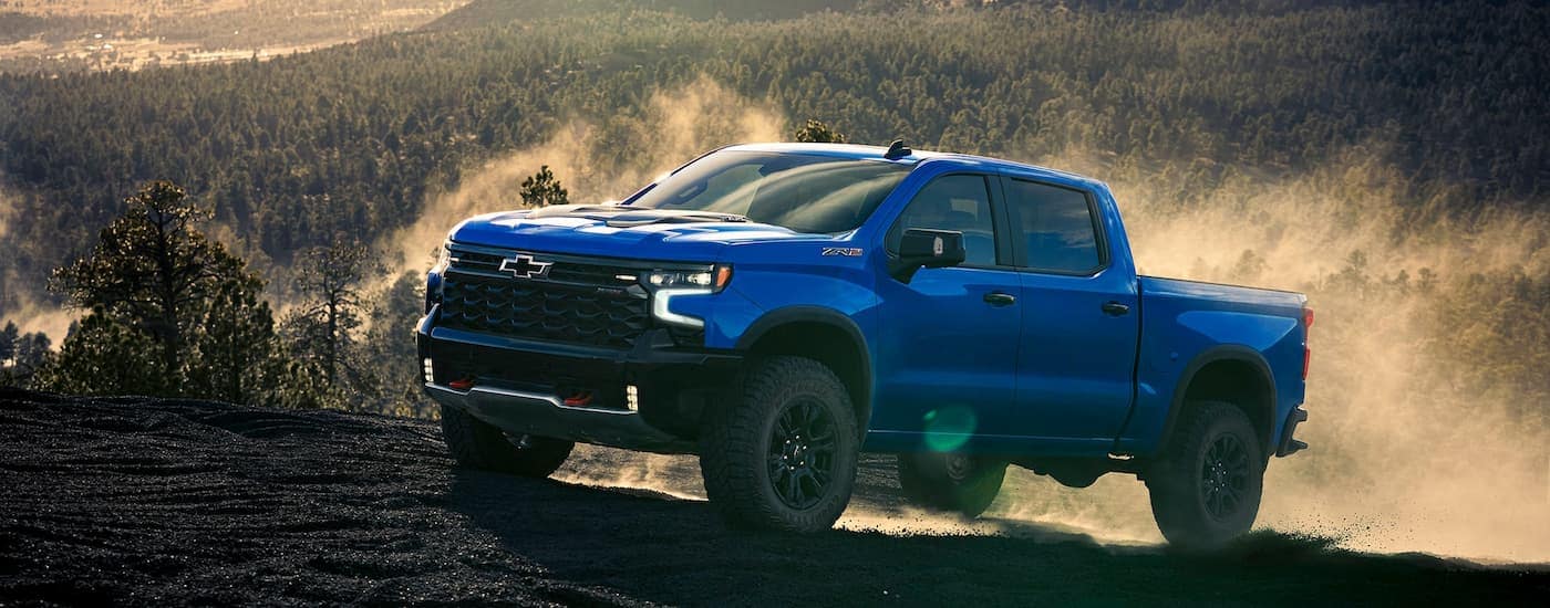 Blue 2025 Chevy Silverado 1500 ZR2 driving up a dirt hill after visiting a dealer with trucks for sale near Wake Forest.