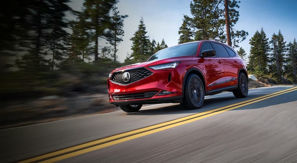A red 2024 Acura MDX is shown driving on a highway.