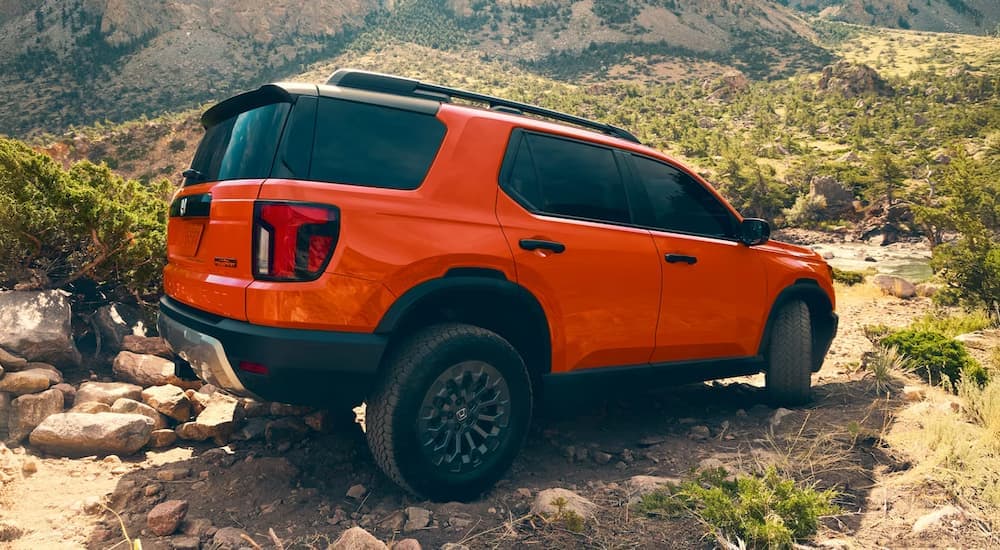 Rear of an orange 2026 Honda Passport TrailSport driving off-road.
