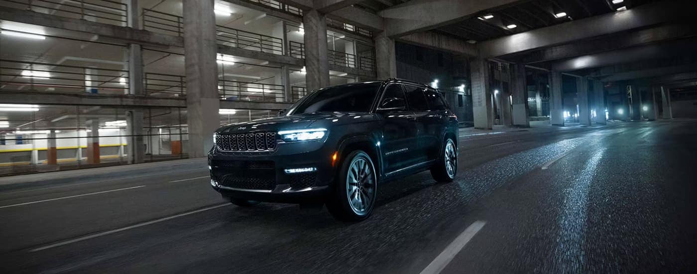 A black 2025 Jeep Grand Cherokee is driving through a city at night.