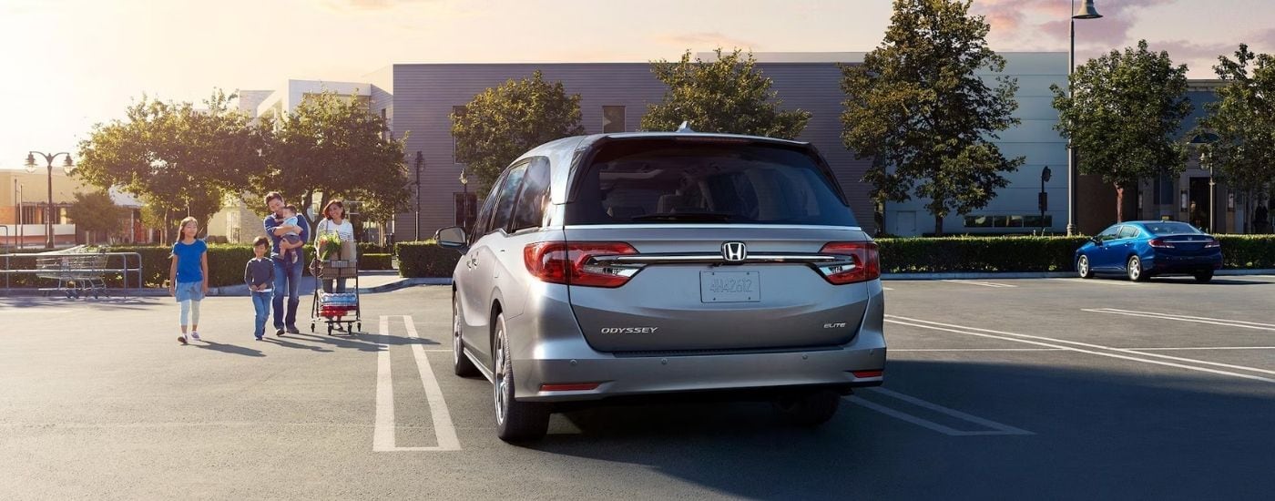 A family walking towards a silver 2024 Honda Odyssey on a parking lot with used cars for sale in Raleigh.