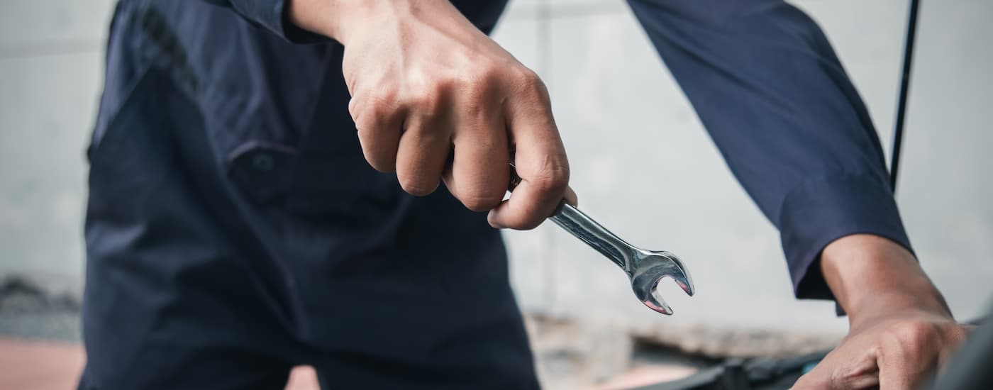 A close up of a mechanic holding a wrench working on an engine.