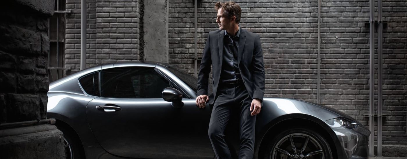 A person is shown leaning against a silver 2022 Mazda MX-5 Miata RF.