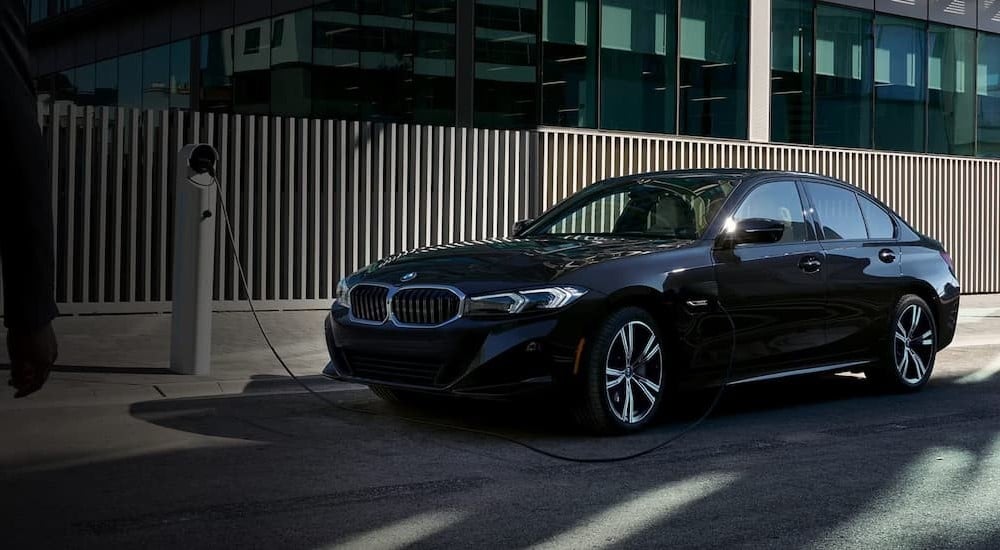 A blue 2024 BMW 3 Series PHEV is shown parked and charging.