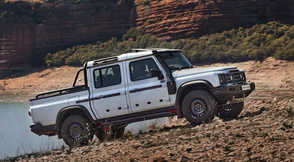 A white 2025 INEOS Grenadier Quartermaster is parked near a lake.