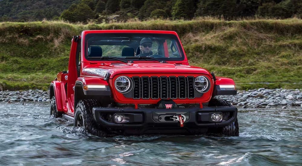 Red 2024 Jeep Wrangler fording a shallow river.