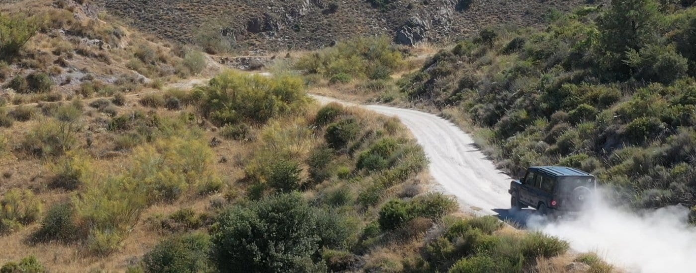 A black 2025 INEOS Grenadier Station Wagon is shown kicking up dust off-road.