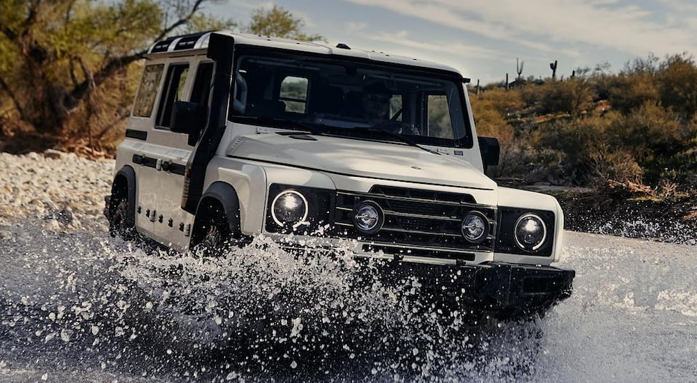 White 2025 INEOS Grenadier for sale near Wilmington driving over a shallow lake.