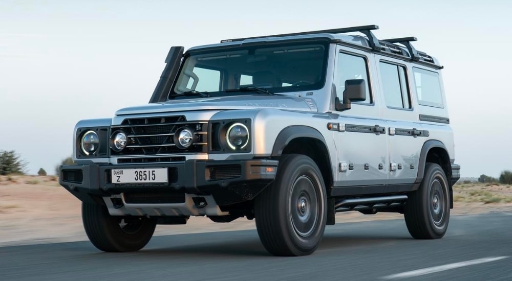 A grey 2025 INEOS Grenadier Station Wagon is shown driving to an INEOS dealer.