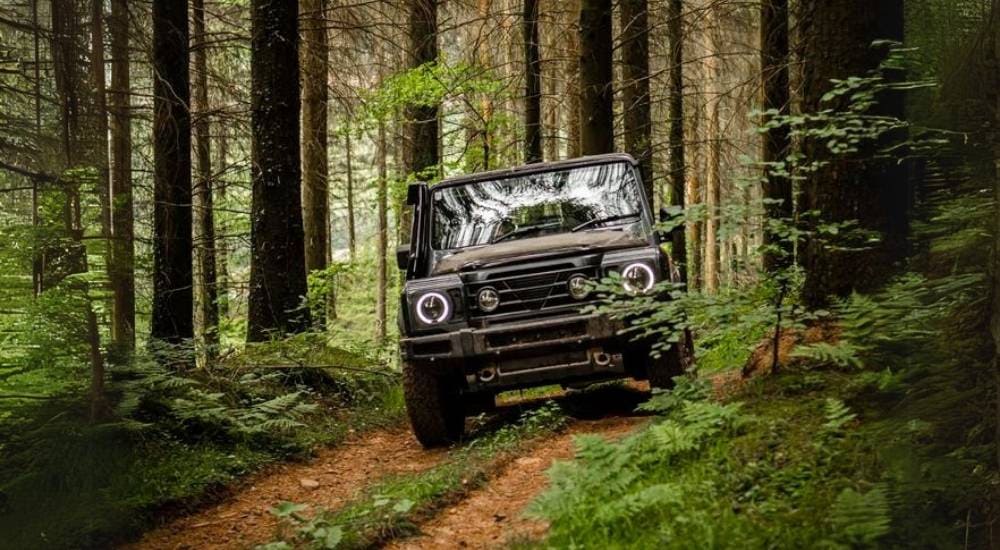 A grey luxury SUV for sale, an INEOS Grenadier, driving in a forest.