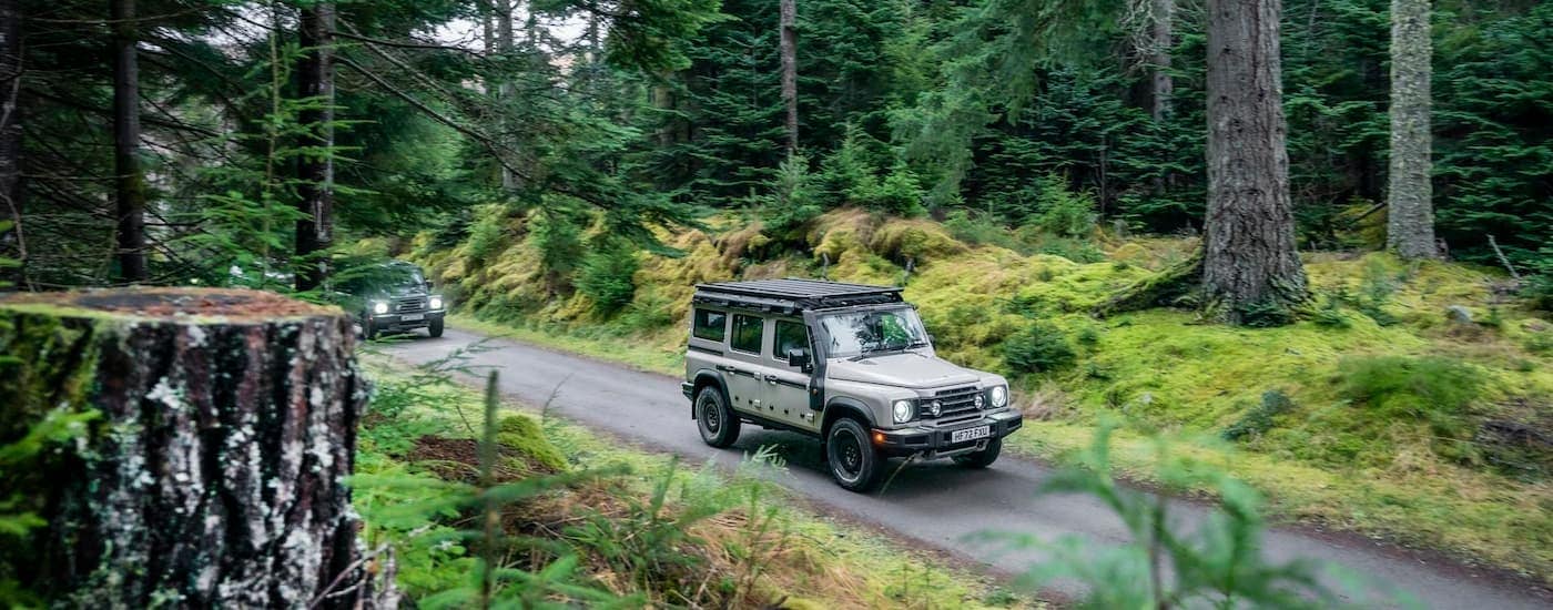Grey Ineos Grenadier driving on a forest road.