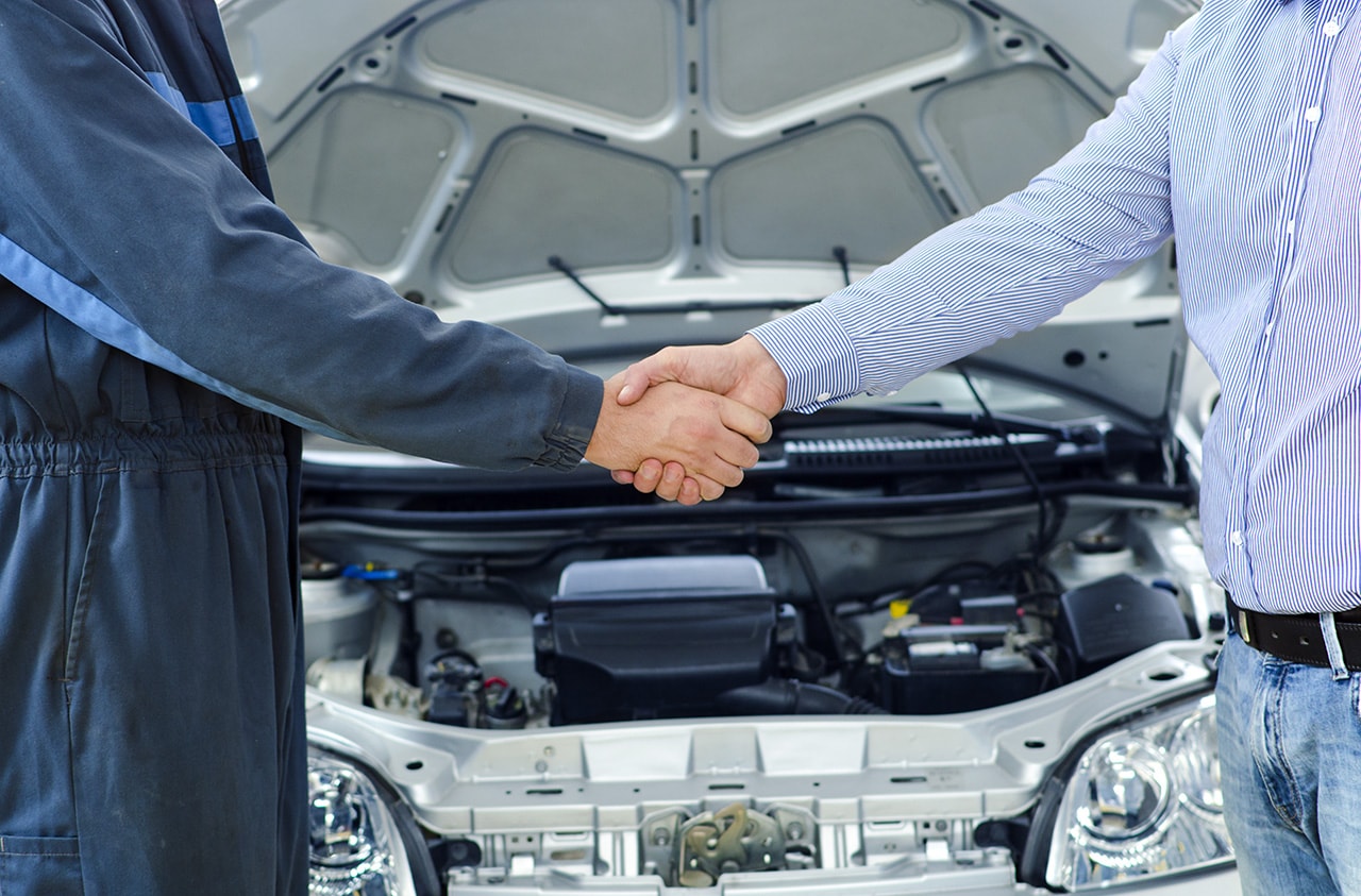 Mechanic and car owner shaking hands in front of vehicle
