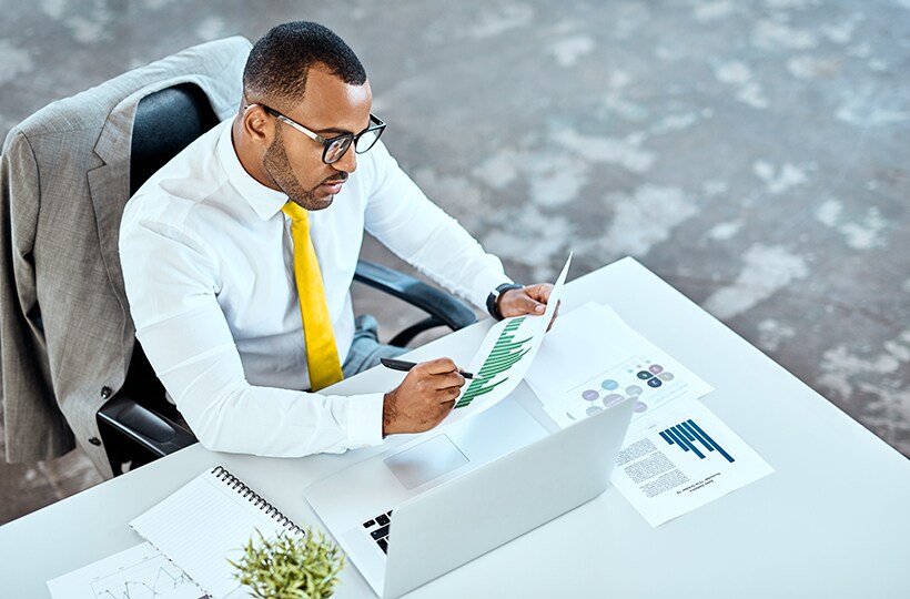 A man looking over printed documents with his laptop open