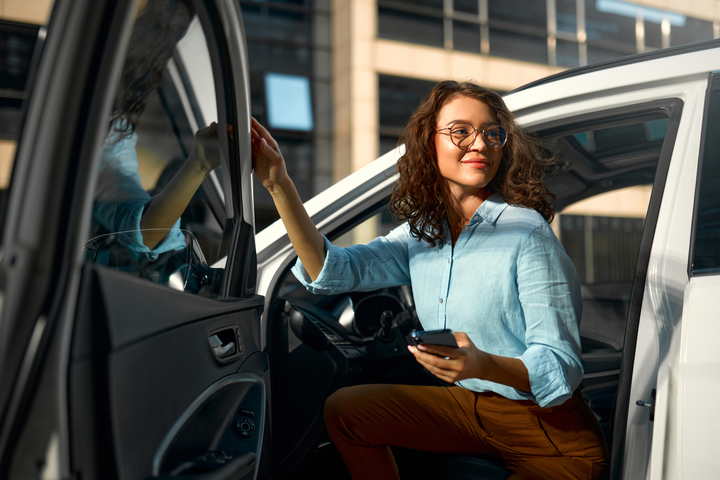  Woman exiting the driver seat of a car with a phone in her hand