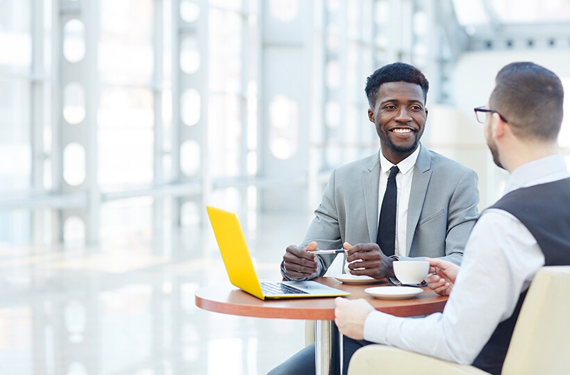 Two men sitting at a table sharing tea with an open laptop between them