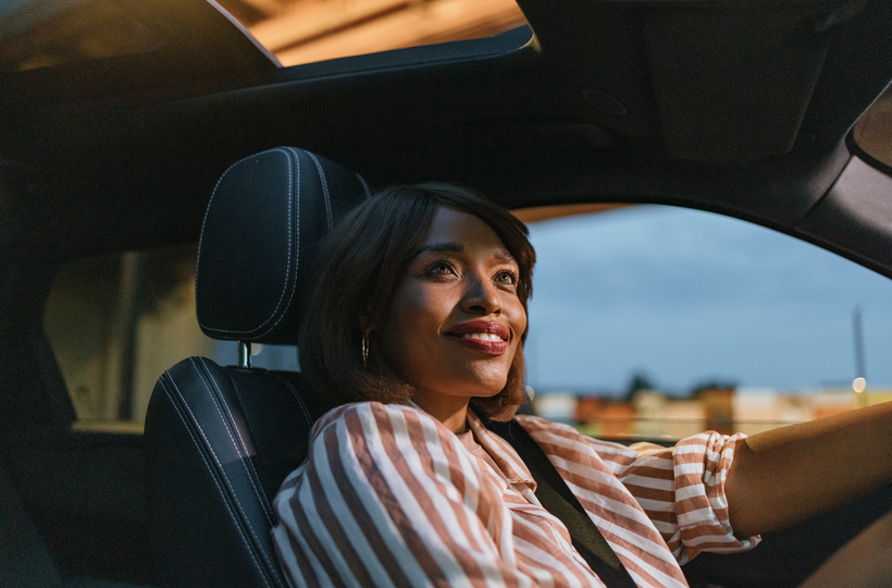  Businesswoman driving a car through the city at dusk with setting sun