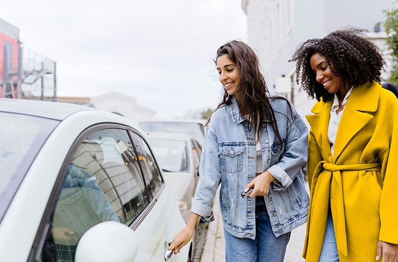 Two women standing next to a car on the street