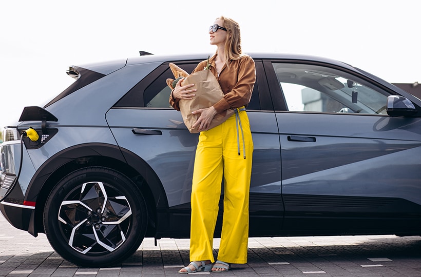  Woman holding a bag of groceries while her electric vehicle charges
