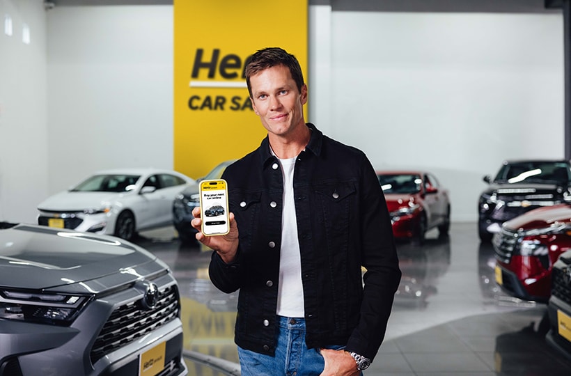  Tom Brady holding up a phone surrounded by vehicles