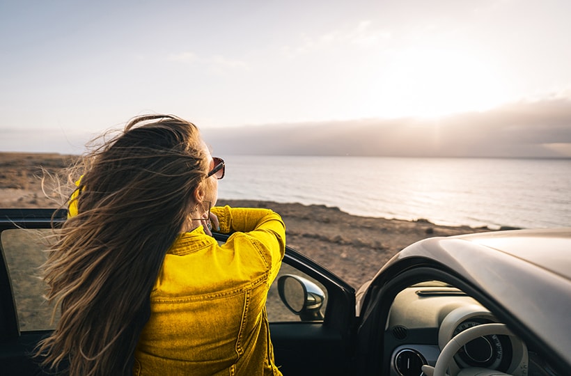 Woman leaning against car door looking at the sunset