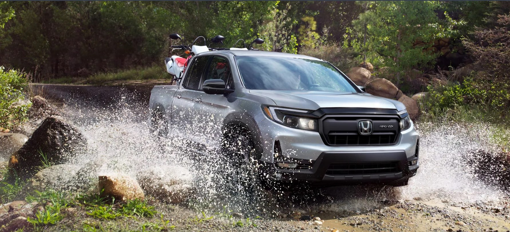 A silver Honda Ridgeline driving on a muddy road in the mountain woods.