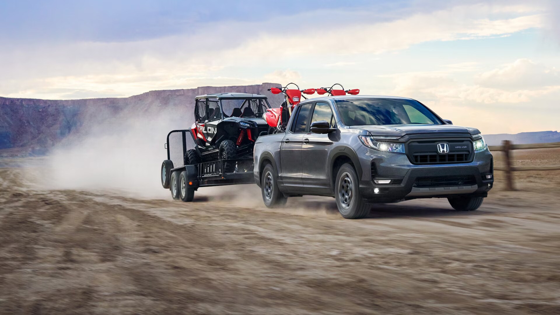 A dark gray Honda Ridgeline towing a razor 4X4 in a western American desert.