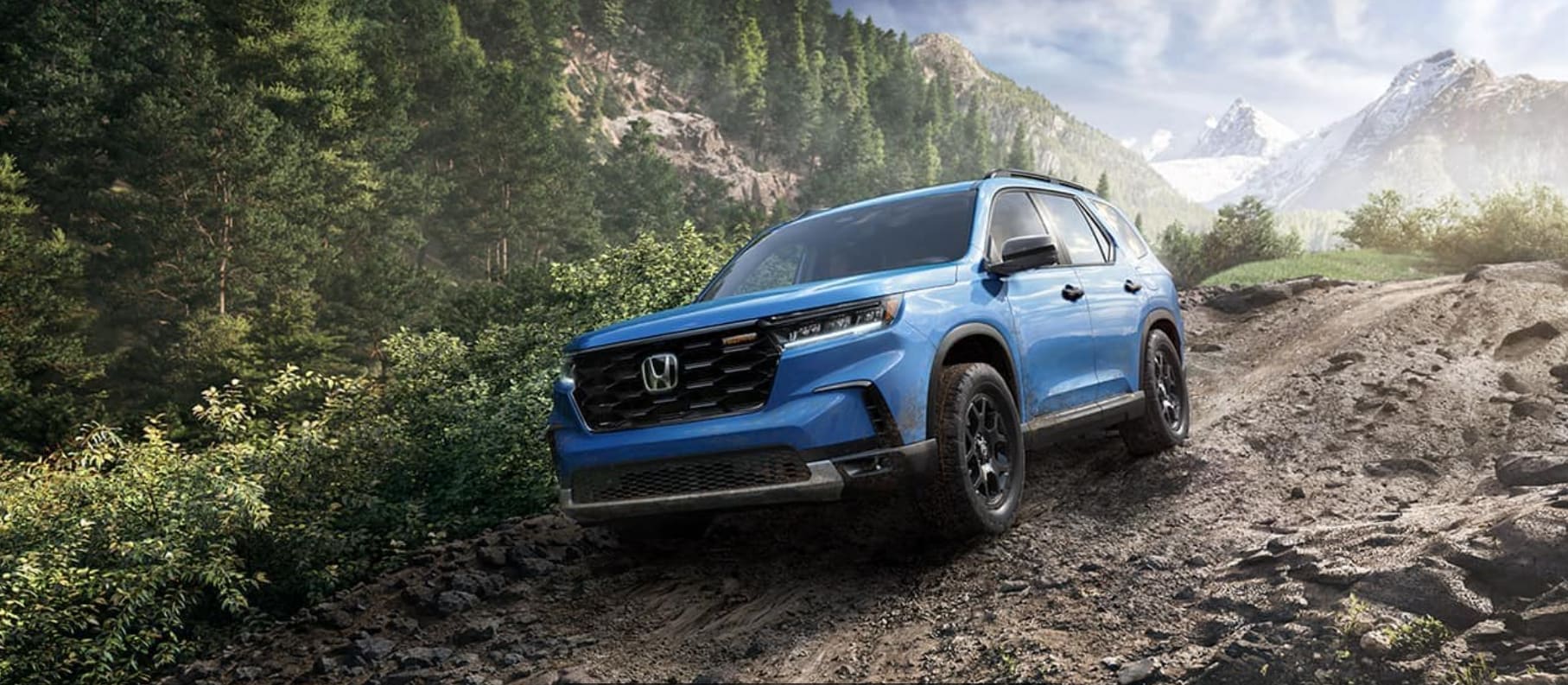 A blue 2023 Honda Pilot drives on a rough off-road trail