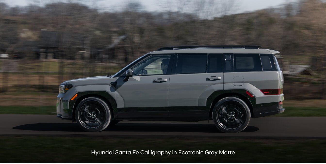 Hyundai Santa Fe Calligraphy in Ecotronic Gray Matte with roof side rails on paved road.