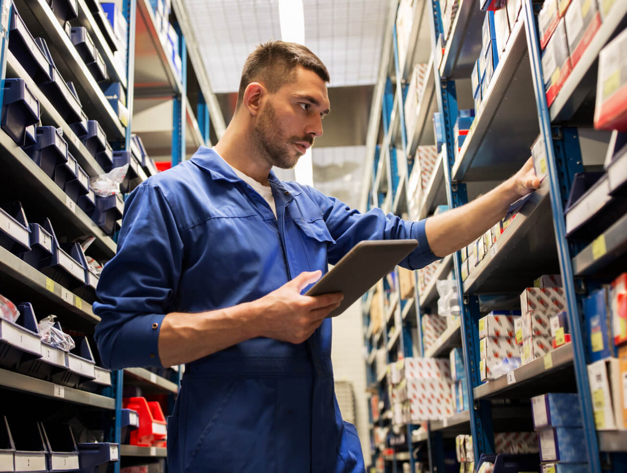 A man in a blue jumpsuit browses auto parts on a shelf.