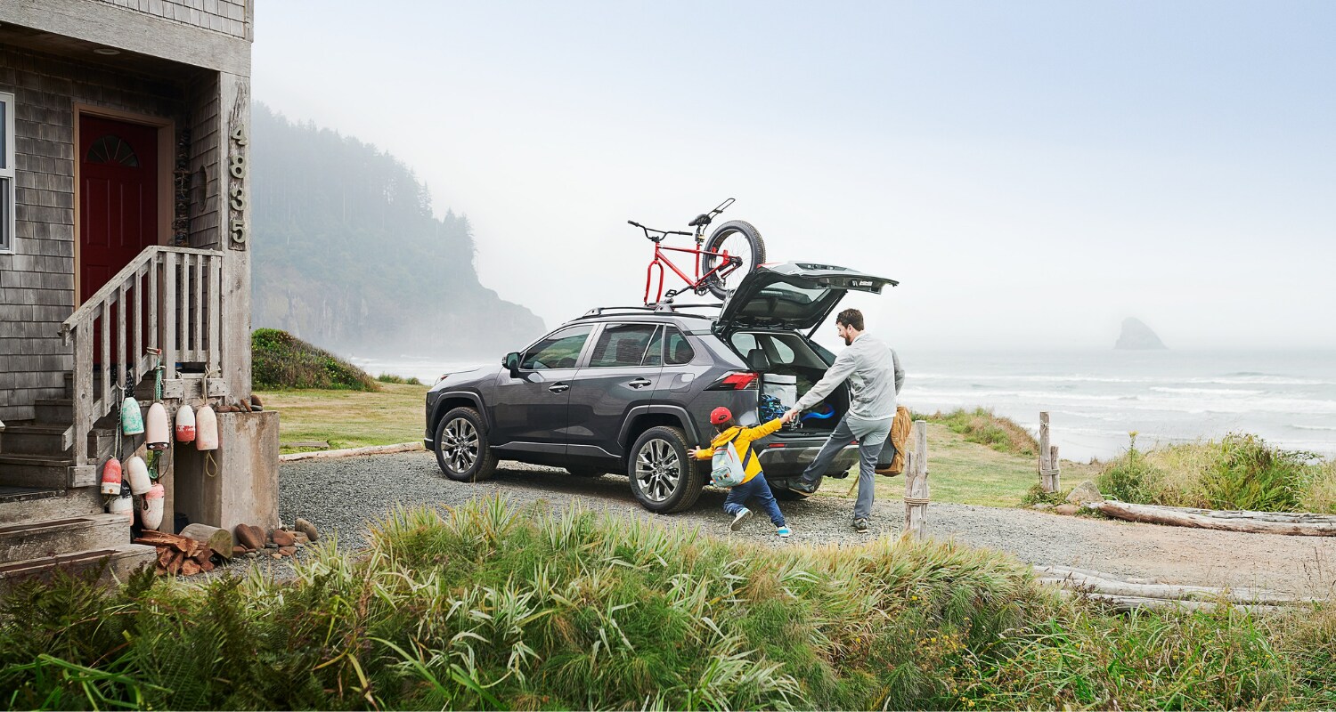 Rear exterior angle of the 2021 RAV4 Hybrid SUV as a father and son load up the cargo area for a road trip