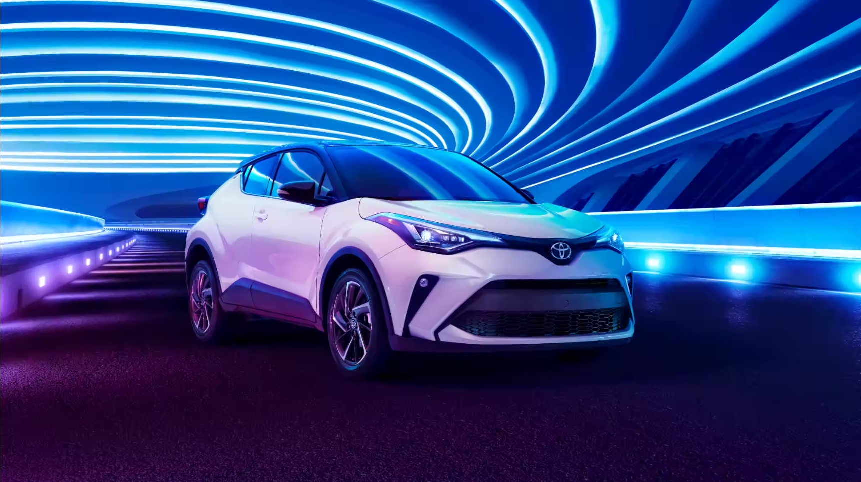 A white 2022 Toyota CH-R sits parked under a series of curvilinear blue lights