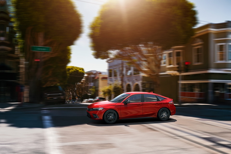 red Honda Civic driving through tree-lined city streets