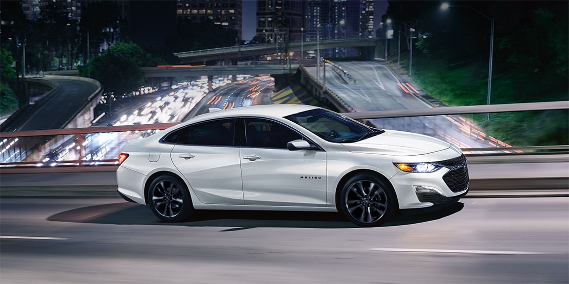 white Chevy sedan driving through a city at night