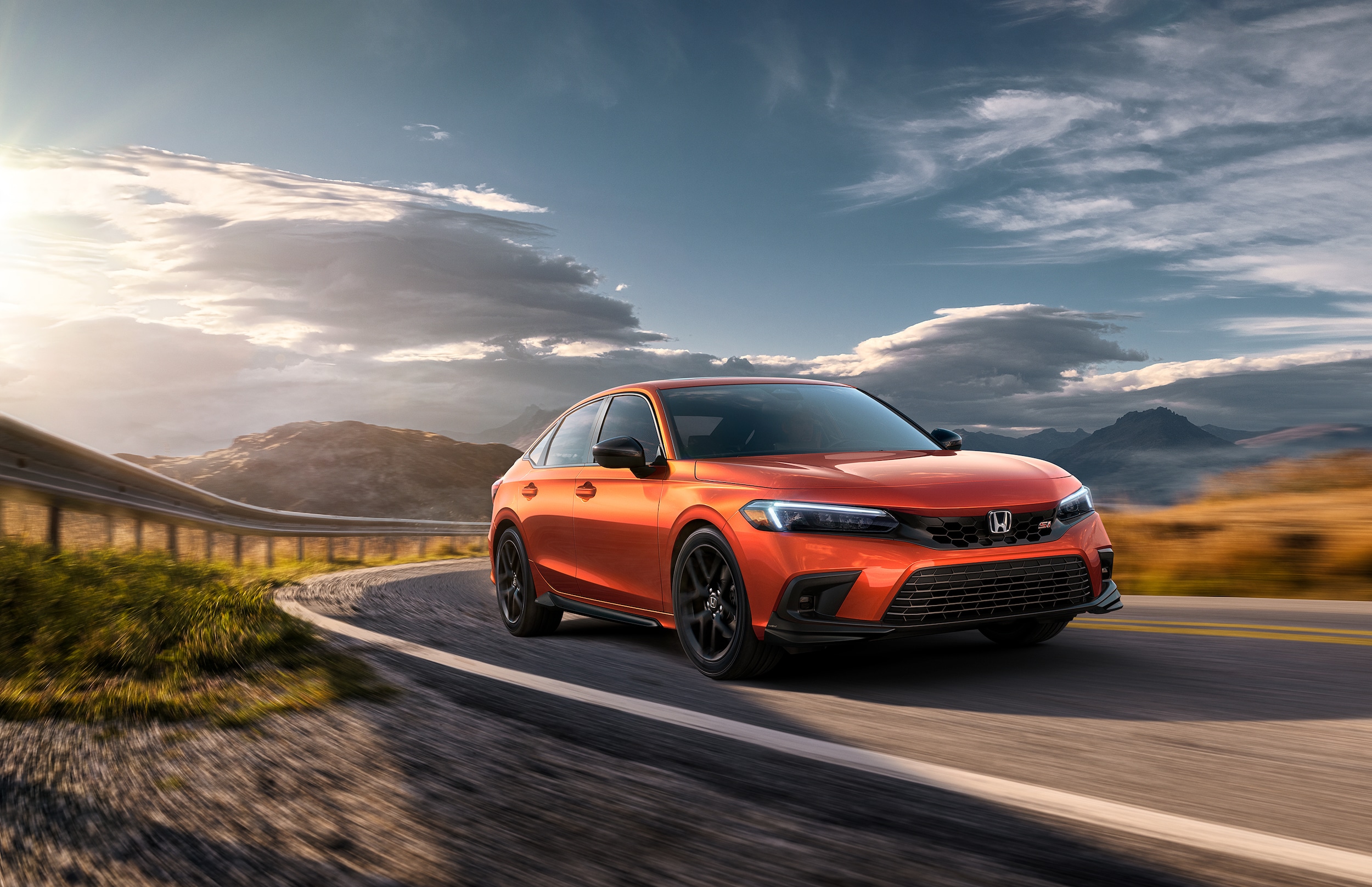 orange Honda Civic Si driving fast down a road with cloudy blue skies