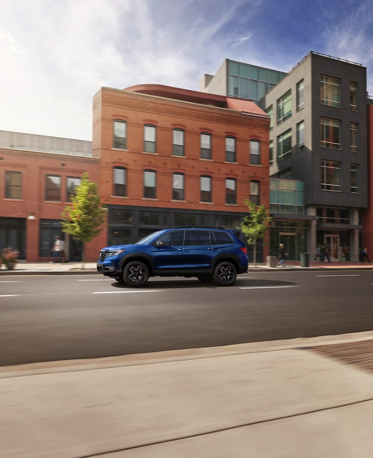 blue Honda Passport SUV driving past a brick building