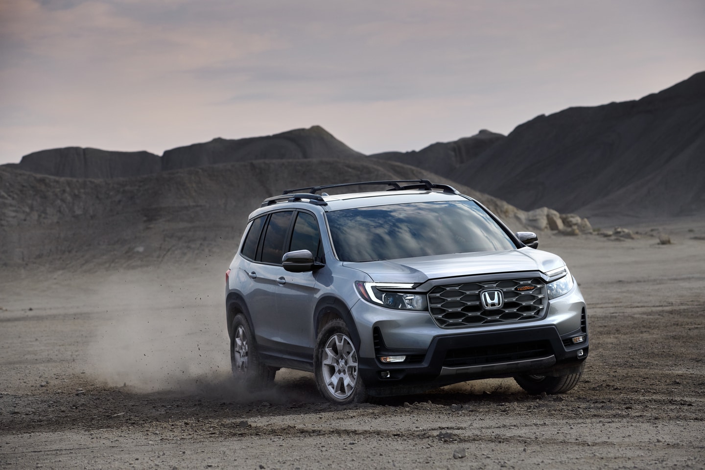 silver Honda Passport driving through a dirt field
