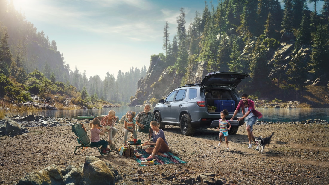 2025-Honda-Pilot-TrailSport-SUV-L07.png grey Honda Pilot parked by a lakeside with a family around