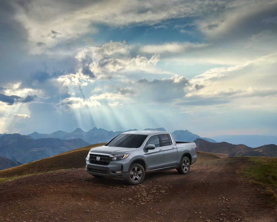 2025-Honda-Rigdeline-RTL-CrewCab-Truck-L02.png silver Honda Ridgeline driving on a dirt hill with sun and clouds above