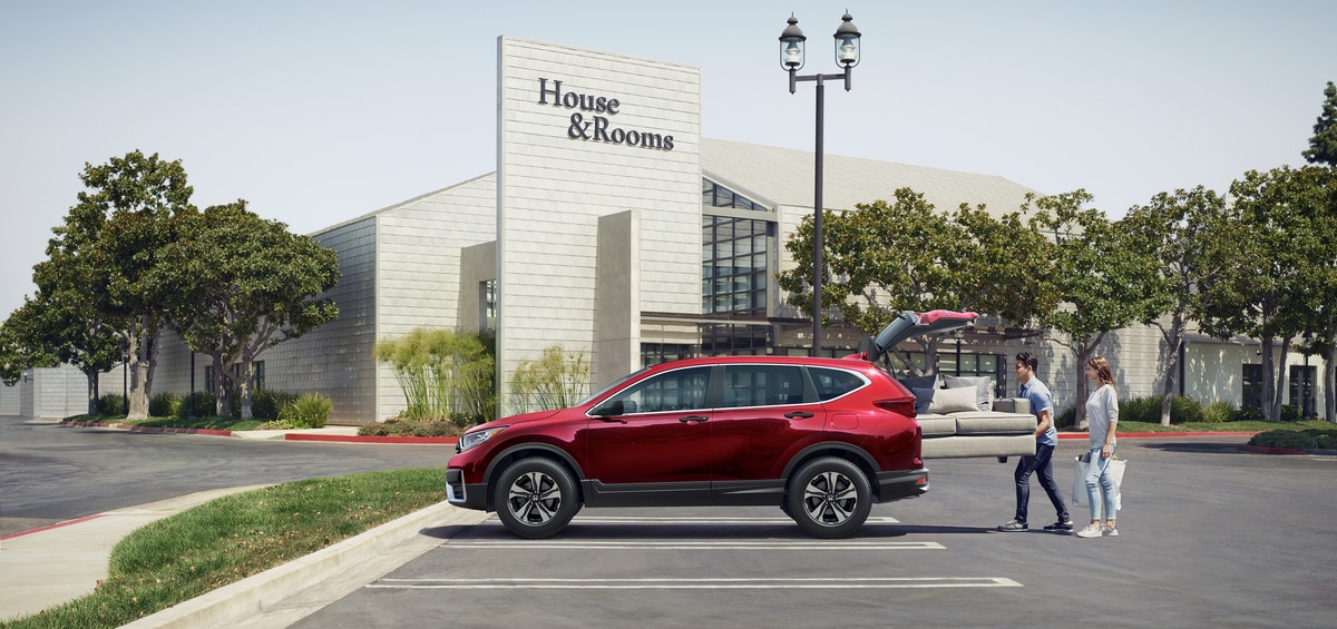 red Honda CR-V SUV in a parking lot, with a couch being loaded in the trunk