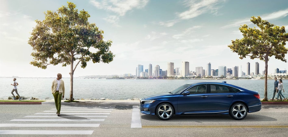 blue Honda Accord Sedan parked at a stop sign, next to a waterfront, with onlookers