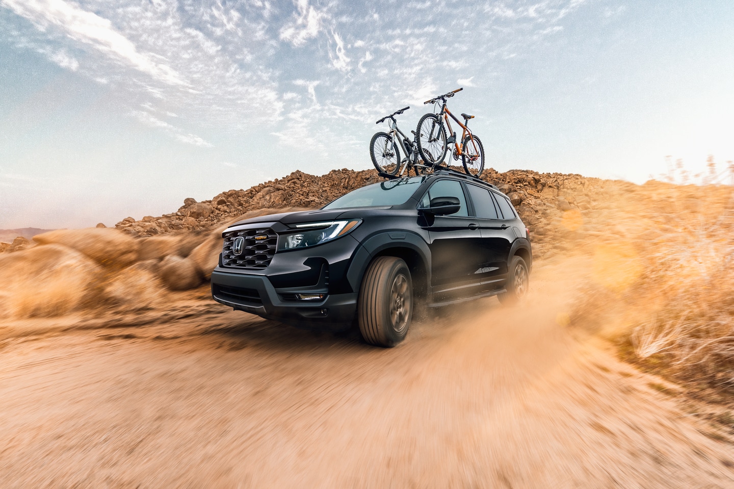 black Honda Passport driving through a sandy desert with bikes on the roof rack